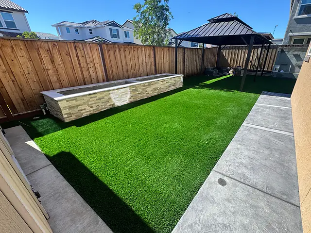 Backyard by CM Hardscape with artificial turf, a stacked-stone planter box, a gazebo and a walkway