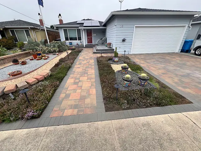 Paver walkway with a charcoal border through a front garden, with a paver driveway beside it