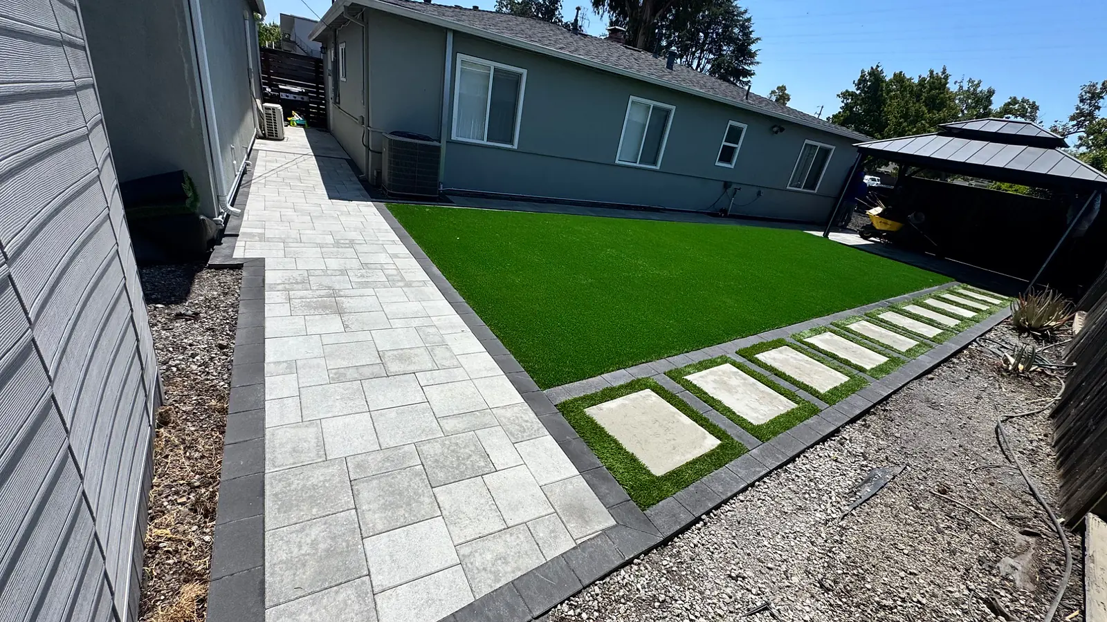 Paver walkway with a charcoal border beside turf and cast concrete stepping pads, built by CM Hardscape