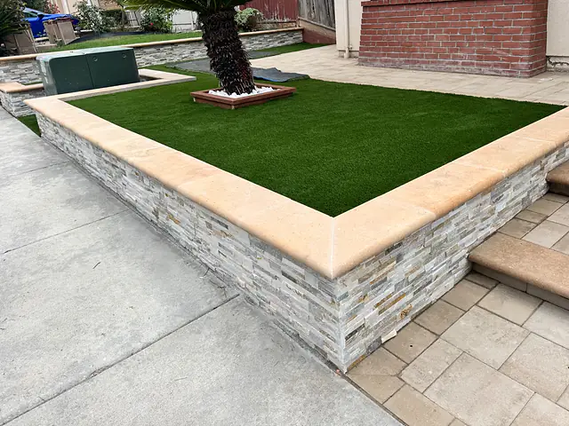 Stacked-stone retaining wall with a precast cap holding a raised turf bed